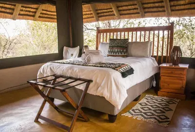 a bedroom with a bed and a table and windows at NIANI tented Chalet in Hoedspruit