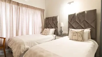 a bedroom with two beds with white sheets and a window at Gaza Homes Self Catering Apartments in Nelspruit