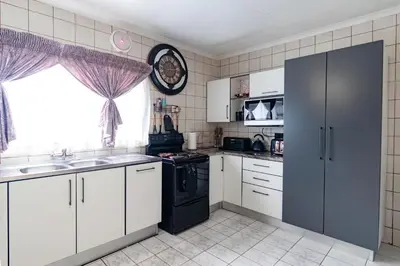 a kitchen with white cabinets and a black refrigerator at Gaza Homes Self Catering Apartments in Nelspruit