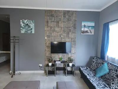 a living room with a couch and a tv on a wall at Le Grix Guesthouse in Nelspruit