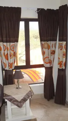 a window with curtains and a table with a lamp at Baobab - NUDE - SunEden Family Naturist Resort in Pretoria
