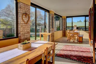 a living room with a wooden table and large windows at Mrs Simpson in Dullstroom