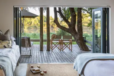 a bedroom with a bed and a patio with a tree at Simbavati River Lodge in Timbavati Game Reserve