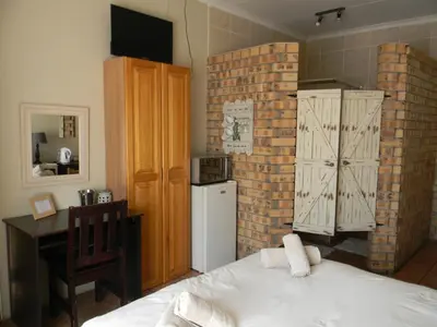 a room with a bed and a desk and a refrigerator at Ridderspoor Guesthouse in Middelburg