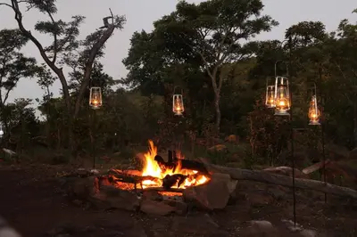 a fire pit with chandeliers and lights in the background at Inzalo Safari Lodge in Welgevonden Game Reserve