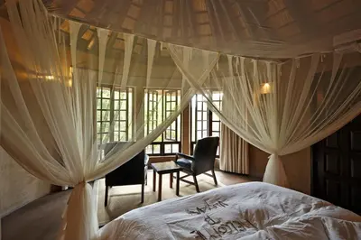 a bedroom with a bed with curtains and a chair at Vuyani Safari Lodge in Hoedspruit