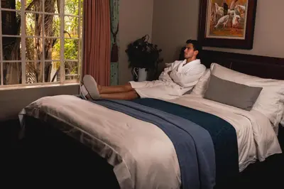 a man sitting on a bed with his feet on the pillow at Village Ridge Stays in Pretoria