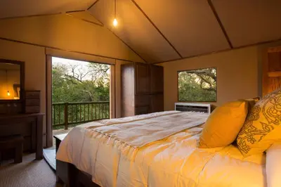 a bedroom with a bed and a balcony with two windows at Vuyani River Lodge in Hoedspruit