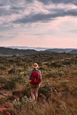 a woman with a red backpack walking through a field at Bateleur Nature Reserve & Stamvrug Hiking Trails in Modimolle