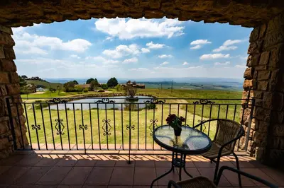 a table and chairs on a balcony with a view of a pond at Gooderson Kloppenheim Country Estate in Machadodorp