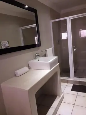 a white bathroom with a sink and a shower at Coyotes Hotel & Conference Centre in Nelspruit