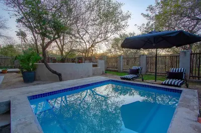 a swimming pool with an umbrella and two chairs and an umbrella at 3433 on Klipspringer Marloth Park Kruger in Marloth Park