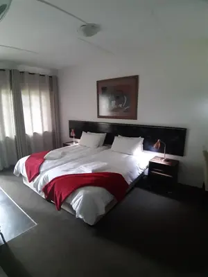 a bedroom with a large bed with white and red sheets at Wayside Lodge in Waterval Boven