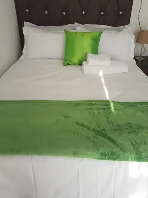 a white bed with green sheets and pillows at MZET GUEST HOUSE in Ermelo