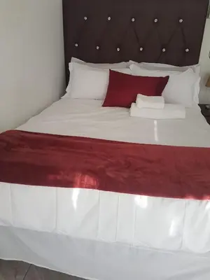 a large bed with red and white sheets and pillows at MZET GUEST HOUSE in Ermelo
