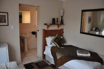 a bedroom with a bed and a bathroom with a mirror at Pilgrims Delight Guest House in Centurion