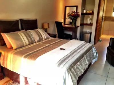a bedroom with a large bed with a desk and a chair at Pilgrims Delight Guest House in Centurion