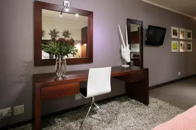 a desk with a vase of flowers and a mirror at Absolute Farenden Apartments in Pretoria
