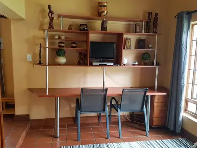a room with a desk with two chairs and a television at Raka Cottage in Nelspruit
