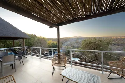 a balcony with chairs and tables and a view at Hinda Mountain Lodge Mabalingwe in Mabula