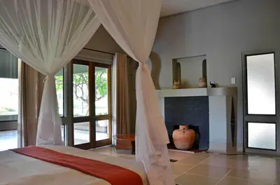 a bedroom with a bed with curtains and a fireplace at Tingala Lodge - Bed in the Bush in Phalaborwa