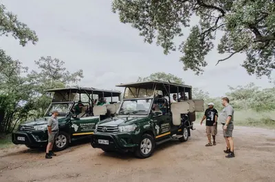 a group of people standing next to two green trucks at Nkambeni Safari Camp in Hazyview