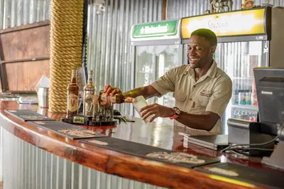 a man standing at a bar making a drink at Nkambeni Safari Camp in Hazyview