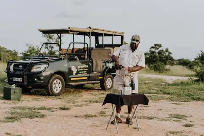 a man standing next to a table in front of a vehicle at Nkambeni Safari Camp in Hazyview