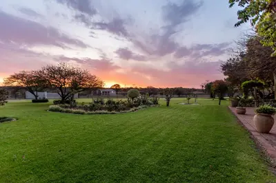 a park with green grass and a sunset in the background at Naledi@53 Private Game Farm in Brits