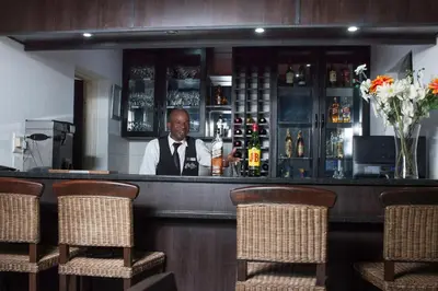 a man sitting at a bar with a bottle of wine at Big Ben Lodge in Polokwane