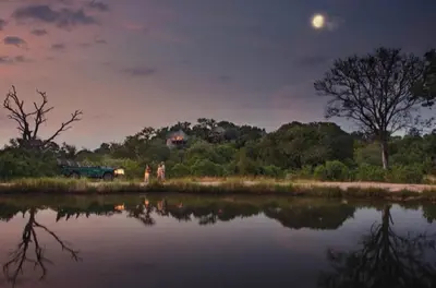 two people standing next to a body of water at night at Leopard Hills Private Game Reserve in Sabi Sand Game Reserve