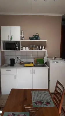 a kitchen with white cabinets and a wooden table with a tableablish at Little Umhlanga in Pretoria