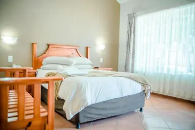 a bedroom with a bed with a wooden headboard and a window at Loskop Valley Lodge in Groblersdal