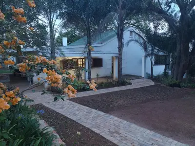 a white house with trees and a brick driveway at Windsor Cottage in Barberton