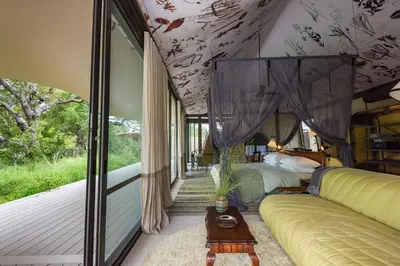 a bedroom with a bed and a couch and a window at Saseka Tented Camp in Hoedspruit