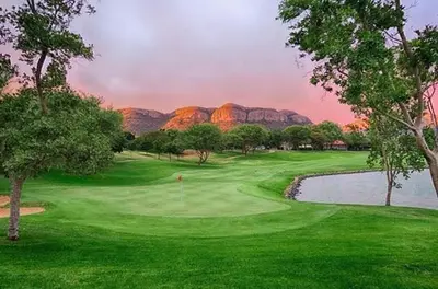 a golf course with a pond and mountains in the background at The Farm in Hartbeespoort