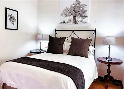 a bedroom with a large white bed with two tables at Brooks Cottage in Pretoria