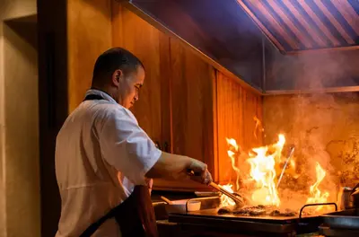 a man cooking food on a grill with flames at Khaya Ndlovu Safari Manor in Hoedspruit