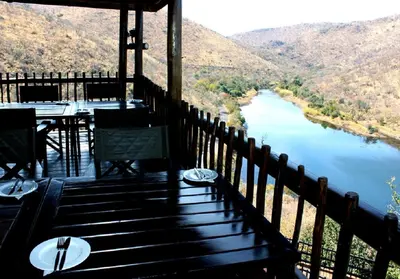 a porch with a table and chairs and a view of a river at Lodge Twentyfour Mabalingwe Nature Reserve in Warmbaths