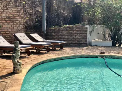 a swimming pool with two chaise lounges next to a brick wall at Summerplace Holiday Home in Hazyview