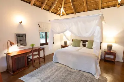 a bedroom with a white bed with a desk and a beduten at Kingly Bush Villa in Phalaborwa