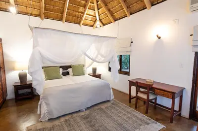 a bedroom with a white bed and a table and a desk at Kingly Bush Villa in Phalaborwa