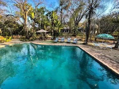 a swimming pool with two chairs and a table at Masasana’s Rest in Hazyview