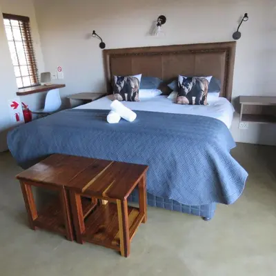 a bedroom with a bed with a blue blanket and a table at Kanaan, Mabalingwe in Mabula