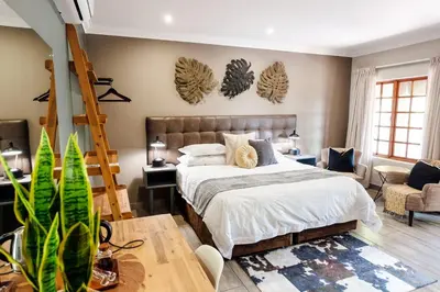 a bedroom with a bed and a couch and a chair at Lowveld Living Guesthouse in Nelspruit