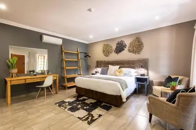 a bedroom with a bed and a desk and chairs at Lowveld Living Guesthouse in Nelspruit