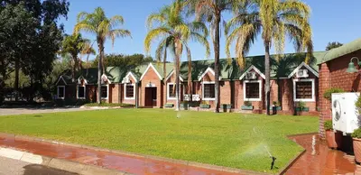 a house with a sprinkler in a yard with palm trees at Pietersburg Club in Polokwane