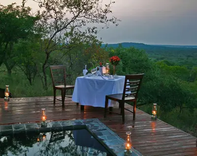 a dining table and chairs on a deck with a pool at Zwahili Private Game Lodge & Spa in Modimolle