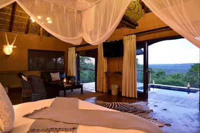 a bedroom with a bed and a living room with windows at Zwahili Private Game Lodge & Spa in Modimolle