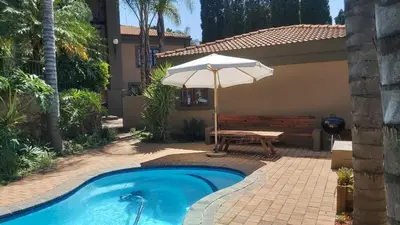 a pool with an umbrella and a table and a bench at Casabac in Pretoria